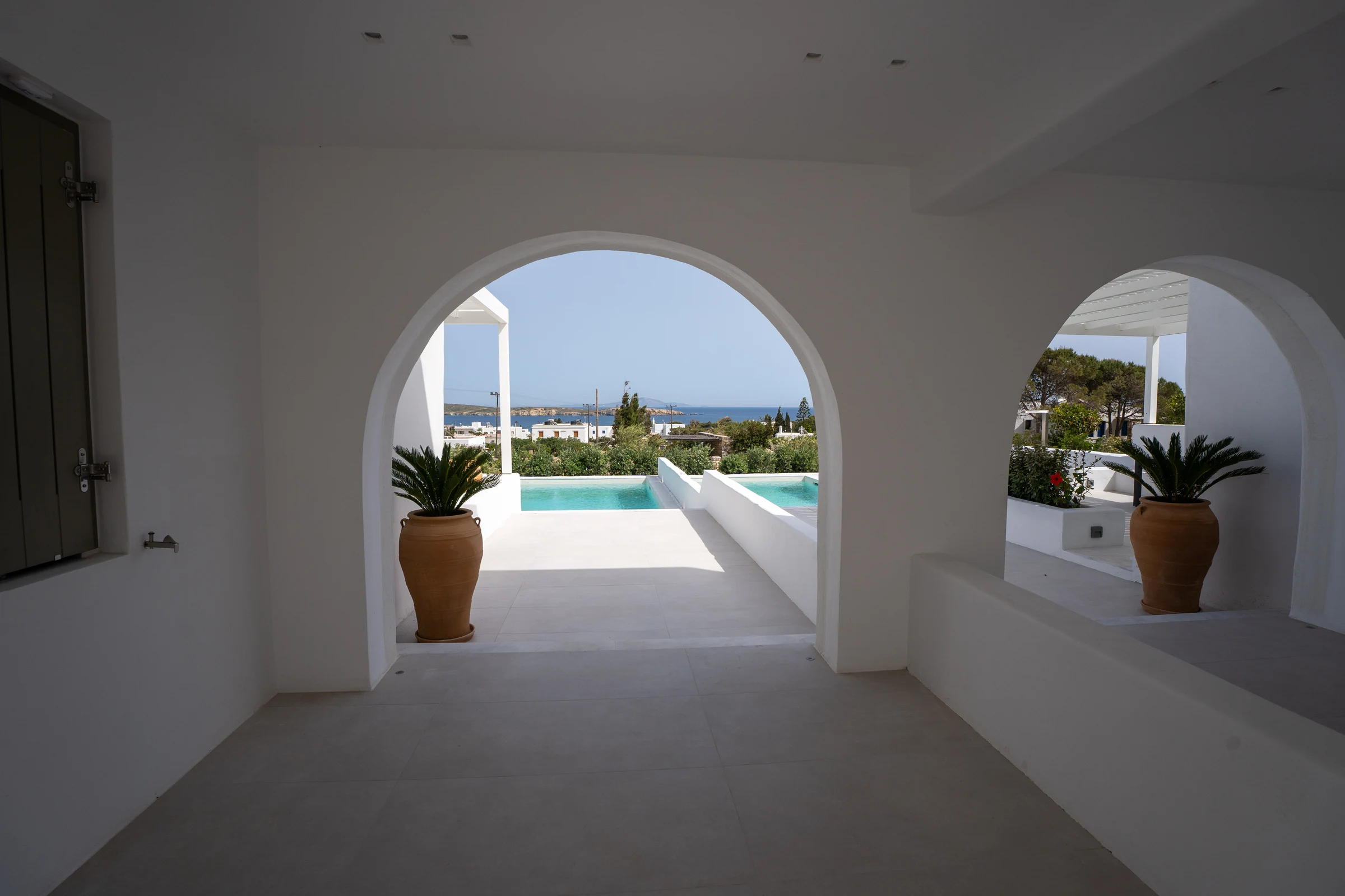 The pools and Aegean seen through the villa’s shaded white arches
